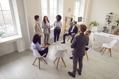 Takım ve koç konuşuyor, çok ırklı ofis çalışanlarından oluşan aktif bir grup beyin fırtınası yapıyorlar, iş stratejilerini tartışıyorlar, fikirler, takım oluşturma aktiviteleri, konferans sırasında profesyonel sohbetler.