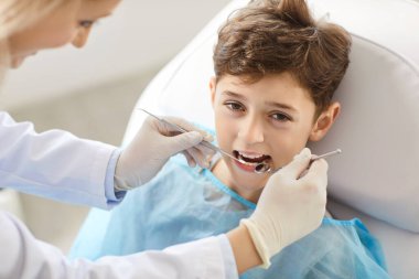 Muayene sırasında diş kliniğindeki mutlu bir çocuğun portresi. Diş hekimi, çocuğun dişlerini incelemek için bir cihaz kullanıyor ve muayene sırasında diş sağlığını sağlama alıyor..