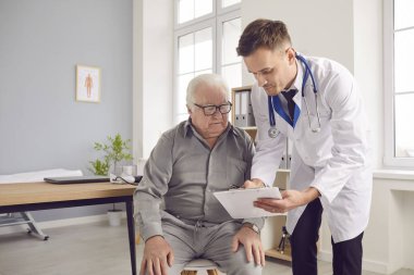 Genç doktor, yaşlı bir adamla ilgilenen erkek hemşire muayeneden önce belgeleri imzalıyor. Hastanedeki ya da klinikteki hasta ya da bakımevinin sakinlerini izleyen, yaşlıların sağlık ve güvenliğini sağlayan adam