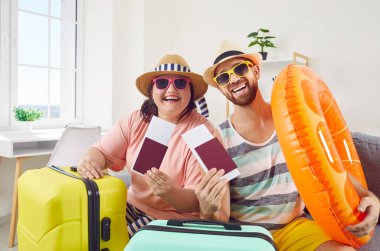 Mutlu, komik, şişman bir çift ve plaj şapkalı, güneş gözlüklü, gülümseyen bir adam tatil gezisine hazırlanıyor. Biletler ve pasaportla evde oturuyor. Tatil ve yaz yolculuğu konsepti.