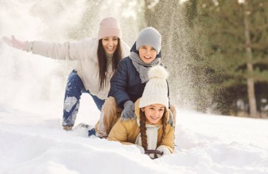 Mutlu gülümseyen anne ve iki çocuk kış parkında kar kaydırağına biniyor. Neşeli çocuklar doğada eğleniyorlar karlı havada aileleriyle birlikte aşağı kayıyorlar. Kış aktiviteleri ve tatil konsepti