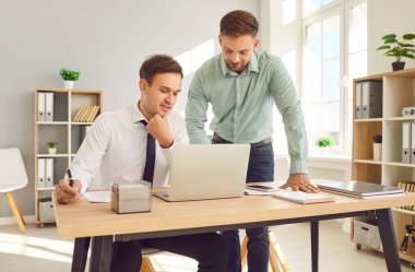 İş yerindeki işadamları. İki genç kendine güvenen işveren toplantı masasında oturmuş dizüstü bilgisayar ekranına bakıyor yeni projeleri ya da girişimleri tartışıyor, şirketi analiz ediyor..