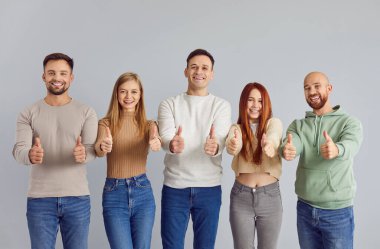 Gri arka planda parmaklarını göstererek ya da birlikte hareket ederek pozitif ve birlik ifade eden gençlerden oluşan çeşitli bir ekip. Bu enerjik grup arasında paylaşılan başarının ve mutluluğun bir sembolü..