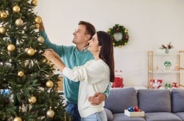 Mutlu bir çiftin portresi Noel ağacını oyuncak toplarıyla süsleyerek evde dikilip kutlamaya hazırlanıyor. Yeni yıl ve kış tatili konsepti.