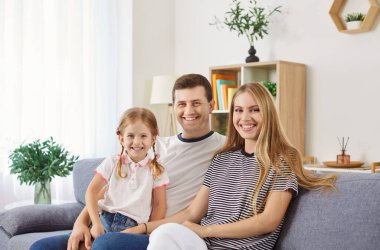 Kanepede oturup kameraya bakan neşeli, güler yüzlü aile portresi. Anne ve baba kızlarını dizlerinin üstüne çöktürüp aile fotoğrafı çekiyorlar. Neşeli anları yakalıyorlar..