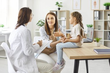 Anne ve küçük kızının hastanedeki bir çocuk doktoru ile tıbbi konsültasyonu var. Randevu sırasında hemşire yardımcı olur, anne ve çocuğa sağlık yardımı yapar..
