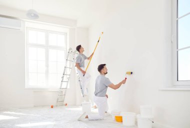 Üniformalı profesyonel ressamlardan oluşan bir ekip boya silindiriyle beyaz duvarı boyuyor. Müteahhitler müşteri evinde tadilat yapıyor. Onarım ve yenileme konsepti.