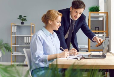 İş yerinde birlikte çalışan iki şirket çalışanı bilgisayardaki muhasebe verilerini inceliyor. Erkek işadamı hesap tablolarındaki rakamlara işaret ederek, meslektaşıyla bilgi tartışıyor..