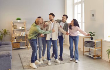 Portrait of a group of laughing happy young friends students or colleagues having fun hanging together at home. Guys and girls standing in a row, hugging and enjoying meeting. Friendship concept.