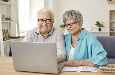 Faturalar, faturalar ve evdeki yatırımlar için dizüstü bilgisayar kullanan yaşlı bir çift. Finans, emeklilik ve borçların düzenlenmesi ve paranın düzgün şekilde idare edilmesini sağlamaya odaklanırlar..