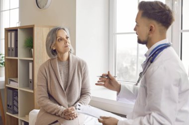 Yaşlı kadın, erkek doktor rehabilitasyon uzmanından rehberlik istiyor. Yaşlı hasta kadın, doktor muayenesinde doktor rehabilitasyoncusunu ziyaret eden yaşlı bir kadını hastaneye yerleştiriyor.