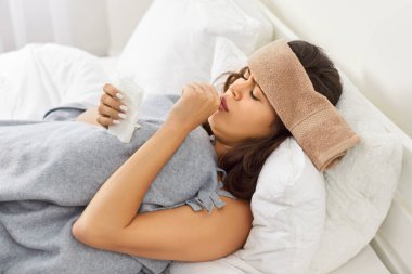 Hasta genç bir kadın, evinde, yatak odasında mevsimsel gripten ya da nezleden dolayı soğuk algınlığından yatıyor. Öksürük ve sıcaklıktan muzdarip sağlıksız bir kadın. Sağlık ve hastalık konsepti.