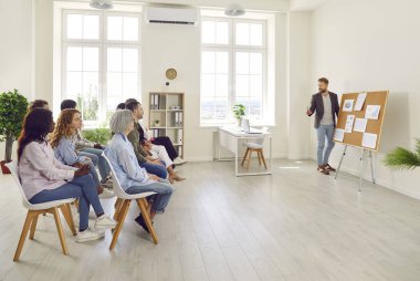 İş arkadaşlarının istatistiklerini ve finansal verilerini diyagram ve grafiklerle gösteren genç ve çekici bir adam konferansta şirket büyümesini analiz ediyor ya da iş eğitimi alıyor..