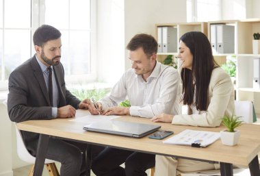 Ofisteki bir toplantıda emlakçı ya da profesyonel danışman ile sözleşme imzalayan pozitif evli bir çift. Müşteri hizmetleri, finansal yatırımlar ve iş güvencesi.