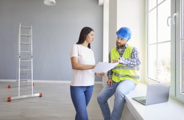 Kadın ve ciddi başarılı profesyonel tamirci düz plan belgelerini değerlendirmek, bakım bilgilerini paylaşmak, işbirlikçi inşaat projesini planlamak, boyayı seçmek, tasarım 