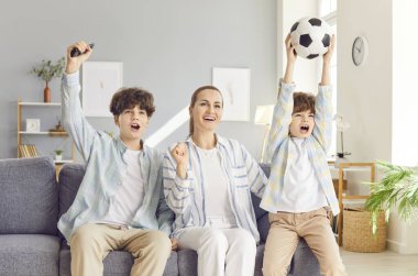 Mutlu genç anne çocuklarıyla kanepede oturuyor ve evdeki oturma odasında TV 'de futbol maçı izliyor. Aile destek spor takımı futbol maçında gol attıktan sonra sevinçle eğleniyor.
