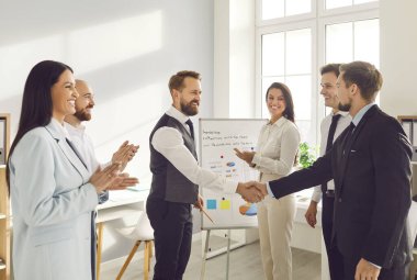 Şirket çalışanları başarıyı kutlamak için el sıkışıyor, anlaşma yapıyor, iş başarısı sağlıyor ya da sözleşme imzalıyor. Bir grup iş adamı bir toplantıda iş arkadaşlarını alkışlıyor..