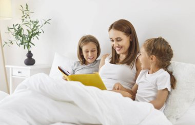 Anne, çocuklarla yatakta kitap okuyor, aile yatak odasında birlikte vakit geçiriyorlar. Konforlu ev ortamında, birlikte kitap okuyarak geçirilen sakin bir sabahta bağ kurulması vurgulanıyor..