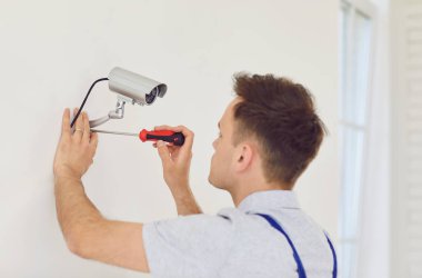 Üniformalı genç teknisyen güvenlik kameralarını evin içine yerleştiriyor. Modern ofiste ya da evde güvenlik kameralarını tamir ederken erkek işçi tornavida kullanıyor. Güvenlik kavramı.