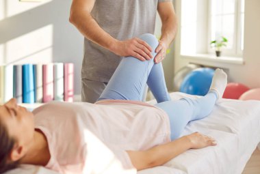 Erkek doktor osteopat ya da fizyoterapist klinikte genç bir kadının dizini muayene ediyor. Hastayla çalışan bir fizyoterapist. Fizyoterapi ve fizik tedavi konsepti.