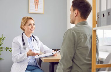 Hastane ziyareti sırasında erkek bir hastayla iletişim kuran pozitif kadın doktor ya da hemşire. Bu tıbbi etkileşim hastaya sağlık ve ilaç yardımı sağlama odaklı.