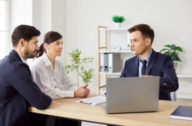Üç ciddi iş adamı ya da iş arkadaşlarından oluşan bir grup masada oturmuş, iş yerindeki iş projelerini tartışıyorlar, dizüstü bilgisayar kullanıyorlar ve birbirlerine bakıyorlar. Şirket çalışanlarının ofiste toplantısı var..