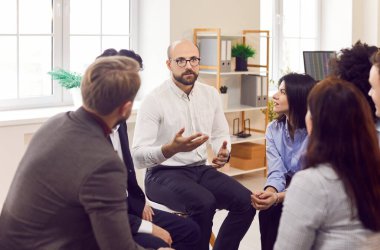 Yetişkin bir adam grup terapi çemberinde fikir paylaşımı için arkadaşlarıyla motivasyon eğitimi hakkında konuşuyor. Daire içinde oturan, konuşan, sorunlarla başa çıkmak için sohbet eden çeşitli insanlar. Psikolojik destek. 