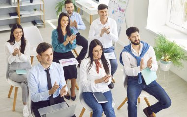 İş konferansında sandalyelerde oturan mutlu, gülümseyen profesyonel seyircinin yüksek açılı çekimi veya şirket iş toplantısı ve iyi bir sunumdan sonra alkışlar.