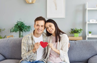 Sevgililer Günü 'nü ya da evde yıldönümünü kutlarken ellerinde kırmızı bir kalp tutan evli çifti sevmek. Romantizm, aşk ve mutluluk, bayramı bir hediye ve neşeli bir sevgiyle anmak..