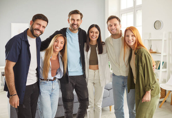 Group portrait of five happy smiling young supportive friends, students or colleagues standing together in row and hugging each other. Радостная группа людей, смотрящих в камеру и делающих групповые фотографии.