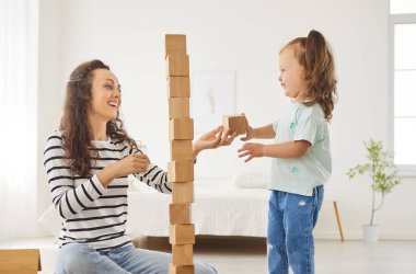 Genç, mutlu, gülümseyen bir annenin portresi. Evde, evdeki oturma odasında eğitici ahşap bir piramit oyunu oynayan tatlı bir kızla yerde oturuyor. Aile ve insanlar kavramı.