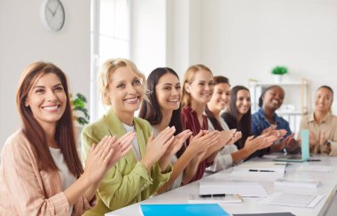 Çeşitli gülümseyen kadınlar konferansta ya da iş eğitimlerinde sıraya girip hoparlörlerini alkışlıyorlar. Toplantıda çok uluslu kadın şirket çalışanları el çırpıyor..