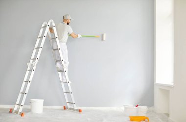 Ressam ya da inşaatçı olarak çalışan profesyonel bir adam, yenileme projesi sırasında duvarları boyamak için tekerlekli fırça kullanıyor. Bir merdiven ile donatıldığında, inşaat ve dönüşüme uzmanlık kazandırır..