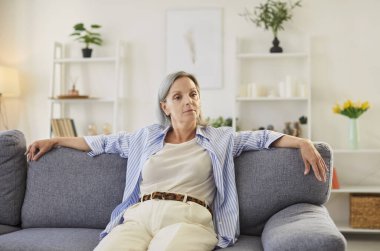 Evdeki kanepede dinlenen son sınıf mutlu bir kadının portresi. Anneanne pozitif ruh hali, rahatlama ve memnuniyet, rahat bir oturma odasında huzurlu bir an sergiliyor.