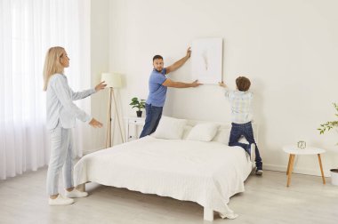 Genç aile sahipleri yeni evlerine taşınıyorlar ve yeni yatak odalarındaki duvara fotoğraf ya da resim asıyorlar. Yeni apartman dekorasyonu yapan çocuklu mutlu ebeveynler. Taşınma veya iç tasarım kavramı.