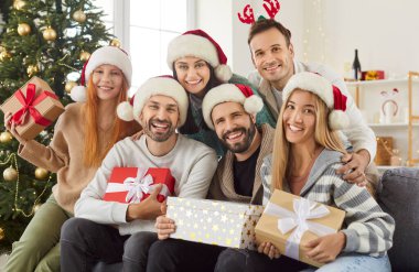 Genç ve mutlu bir insan grubunun portresi evdeki kanepede oturan erkek ve kadın hediye kutularıyla birlikte Noel 'i ya da yeni yılı kutluyor ve kameraya neşeli görünüyor. Kış tatili.