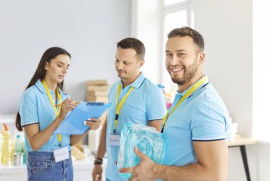 Mutlu erkek gönüllü maden suyu ile birlikte diğer gönüllülerle birlikte çalışıyor. Evsizlere barınak ve mülteci merkezleri sağlayan hayır kurumu için. Bağış konsepti