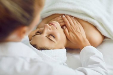 Kadın masör, güzellik salonunda ya da kozmetoloji dolabında gözleri kapalı yatan genç bir kıza omuz ve boyun rahatlatıcı masaj yapıyor. Profesyonel kozmetik uzmanı kaplıcadaki kadına masaj yapıyor..