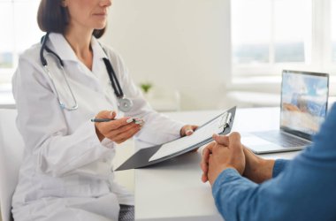 Modern klinikteki doktor genç adamla konuşuyor. Masasında dizüstü bilgisayarla oturan bir doktor hastasına tedavi ve sağlık risklerini anlatıyor. Kesilmiş atış. Tıbbi danışma kavramı