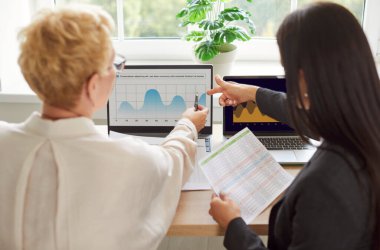 Ofiste bir araya gelen kadın iş arkadaşlarının bilgisayar, belge ve çizelge kullanarak arka planda birlikte çalışmalarına. Muhasebe ve işbirlikçi görevler gösteri takımı verimliliği.