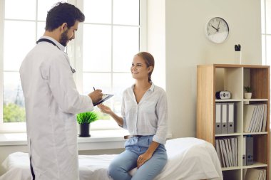 Beyaz üniformalı erkek doktor özel hastane ya da klinikteki kadın hastaya danışıyor. Bakıcı erkek terapist ya da pratisyen hekim gülümseyen kadın müşteriler için reçeteli sağlık kontrolü yapar. Tıp konsepti.