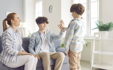 Mutlu gülümseyen kardeşler evdeki oturma odasında anneleriyle beşlik çakıyor. Kadın ebeveyn kanepeye oturmuş, çocukları da var. Aile eğlencesi ve takım konsepti.