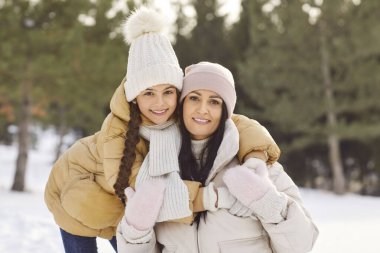 Kış karlı açık hava aile portresi, anne, kız tatilde, sıcacık kıyafetler içinde, kucaklaşan sevimli küçük kız, heyecanlı anne sevgi gösteriyor, şefkat gösteriyor, hafta sonu ormanda yürümekten zevk alıyor.