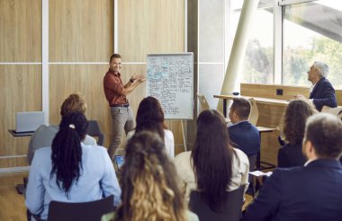 Genç iş adamı toplantı odasında oturan bir grup şirket çalışanının iş projesinden bahsediyor. Çeşitli iş adamları ofiste yapılan bir konferansta şirket büyümesini tartışıyor.
