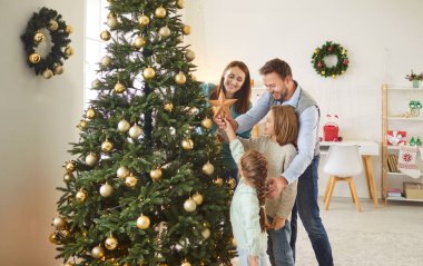 Mutlu genç aile babaları ve çocuklar Noel 'de bir araya gelip evlerini güzelleştiriyorlar. Neşeli baba, anne ve iki çocuk süslenmiş Noel ağacının tepesine altın yıldız koymaya hazırlanıyor..