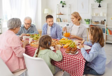 Evde mutlu aile yemeği, büyükanne ve büyükbaba, baba ve iki küçük çocuk oturma odasında, haftasonu anın tadını çıkarıyorlar, gülümseyen ebeveynler birlikte vakit geçiriyorlar, ortak akşam yemeği yiyorlar.