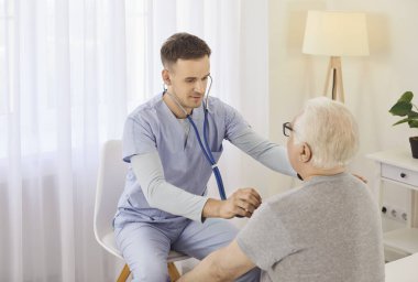 Doktor ya da hemşire yaşlı bir adamın ciğerlerini incelemek ve hastane ortamında nefes almak için stetoskop kullanıyor. Odaklanmış muayene, solunum sağlığı ve kaliteli sağlık hizmetlerini ele alır.