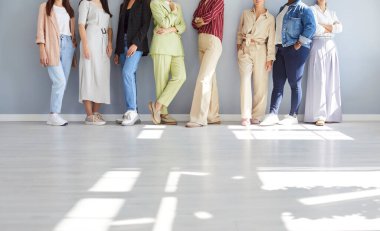 Gri bir arka planda güvenle duran yüzsüz genç kadın grubunun kesilmiş portresi. Kadın arkadaşlar, iş arkadaşları ya da şirket çalışanları, günlük giysiler giyip kapalı alanda sıraya girmişler..