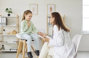 Dost canlısı bir pediyatrist doktorun portresi, klinikteki iş yerinde oturan ve tıbbi muayeneden sonra tavsiyelerde bulunan küçük kız hastasıyla konuşuyor..