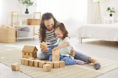 Genç mutlu anne evdeki oturma odasında küçük şirin bir kızla eğitici ahşap piramitlerle oyun oynuyor. Kadın ebeveyn kızıyla vakit geçiriyor. Aile eğlencesi ve insan konsepti.